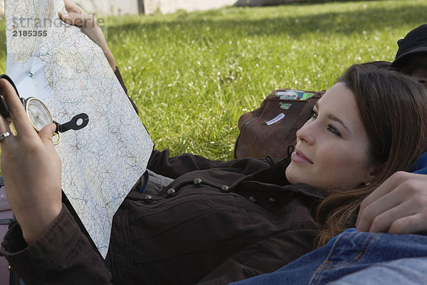 Frau lächelnd haltend Karte liegend auf schlafendem Mann in einem Park.