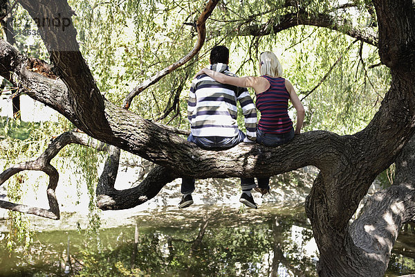 Ein Paar sitzt auf einem Baum am See.