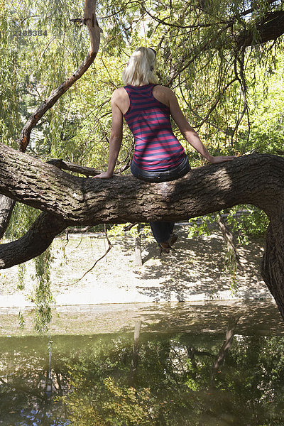 Frau sitzt auf einem Baum am See.