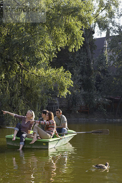 Vier Freunde in einem Ruderboot lächelnd und zeigend.
