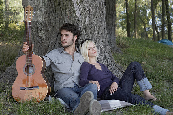 Ein Mann hält eine Gitarre mit einer schlafenden Frau  die sich auf ihn stützt.