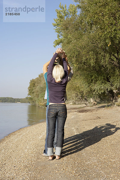 Vier Freunde halten einen Baumstamm am See.