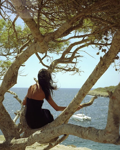 Eine Frau sitzt auf einem Baum mit einer vorbeifahrenden Jacht.