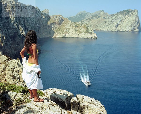 Frau steht auf einem großen Felsen mit einem Schnellboot  das vorbeifährt.