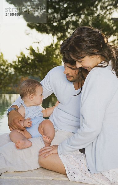 Familie s/baby draußen umarmend und lächelnd.