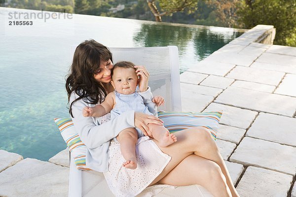 Frau hält ein Baby an einem unendlichen Pool und lächelt.