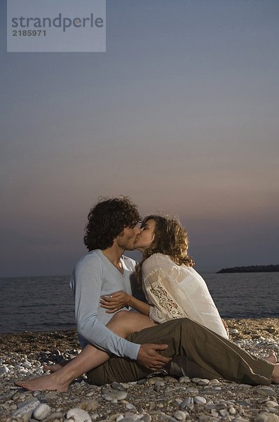 Junges Paar am Strand sitzend küssend  Sonnenuntergang
