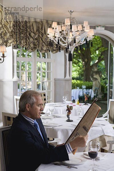 Geschäftsmann beim Mittagessen beim Lesen einer Finanzzeitung