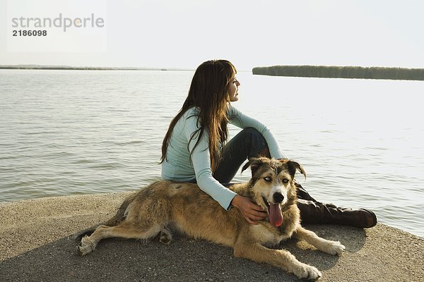 Frau am See sitzend mit Hund.