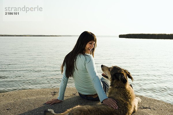 Frau am See sitzend mit Hund.