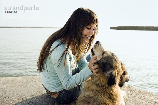 Frau am See sitzend mit Hund.