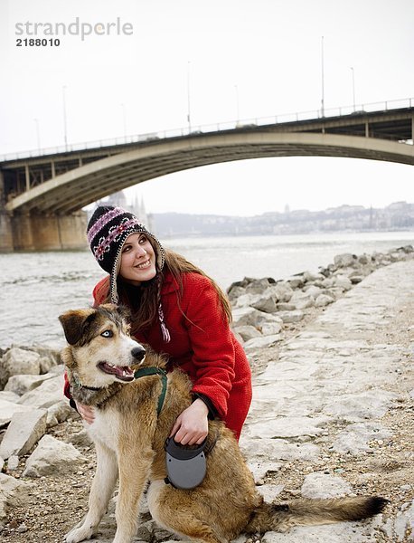 Junge Frau kniend mit Hund am Flussufer  lächelnd