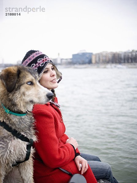 Junge Frau am Fluss sitzend mit Hund (Schwerpunkt Frau)