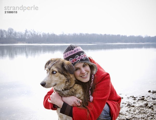 Junge Frau kniend am Fluss umarmend Hund  lächelnd  Portrait