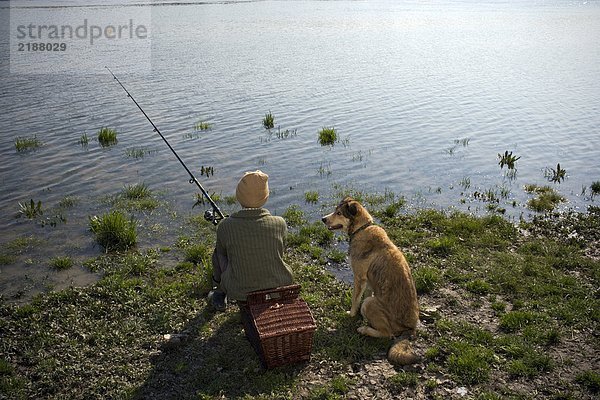 Junge (12-14) Angeln am Fluss mit Hund  Rückansicht