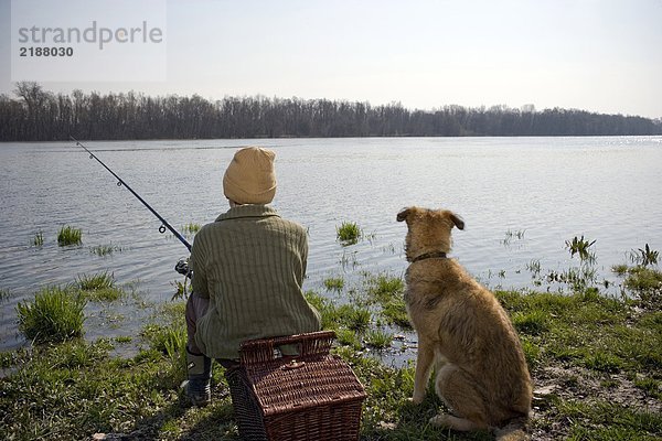 Junge (12-14) Angeln am Fluss mit Hund  Rückansicht