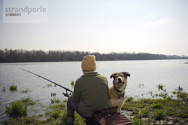 Junge (12-14) Angeln am Fluss mit Hund  Rückansicht