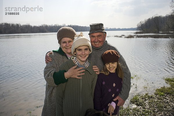 Großeltern am Fluss mit Enkel (12-14) und Enkelin (11-13) lächelnd