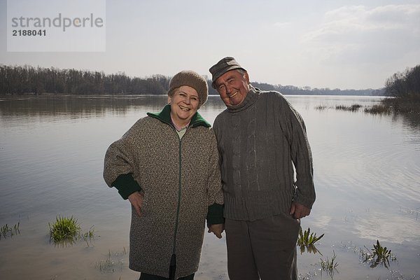 Seniorenpaar am Fluss stehend  Händchen haltend  lächelnd  Portrait