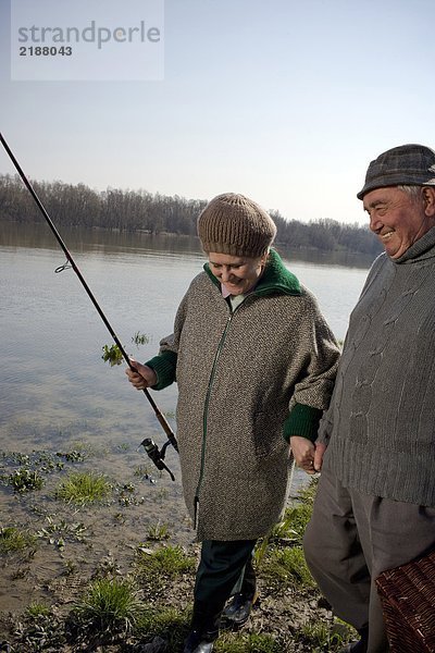 Seniorenpaar am Fluss entlang  Frau mit Angelrute  lächelnd