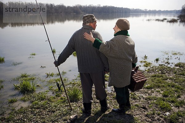 Älteres Ehepaar steht am Fluss  hält Angelrute und Korb