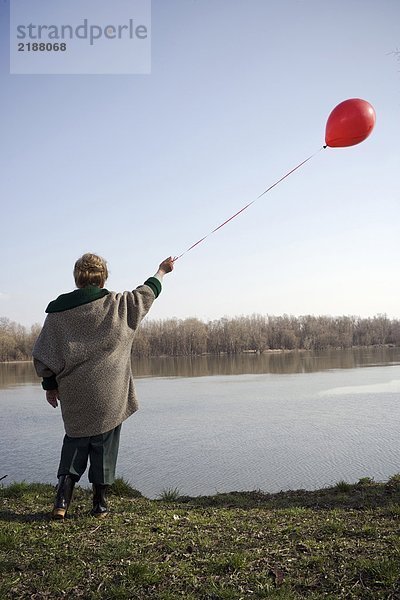 Seniorin am Fluss stehend mit rotem Ballon  Rückansicht