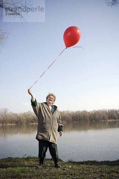 Seniorin am Fluss stehend mit rotem Ballon  lächelnd