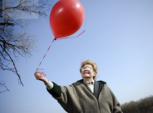 Seniorin im Freien mit rotem Ballon  lächelnd  Blickwinkel niedrig