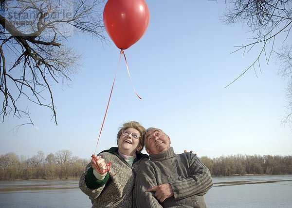 Seniorenpaar am Fluss mit rotem Ballon  lächelnd