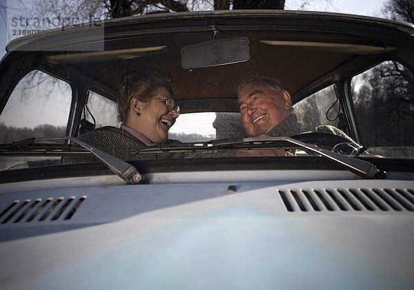 Älteres Ehepaar sitzt im Auto und lächelt sich an