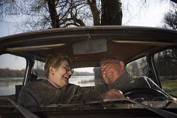 Älteres Ehepaar sitzt im Auto und lächelt sich an