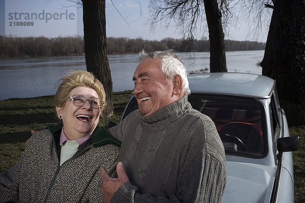 Seniorenpaar steht am Flussufer und lacht.