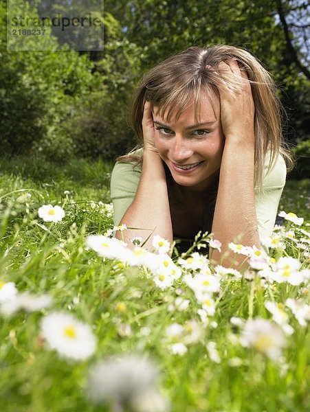 Frau lächelnd im Gras liegend.