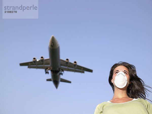Eine Frau  die eine chirurgische Maske trägt  während ein Flugzeug darüber fliegt.