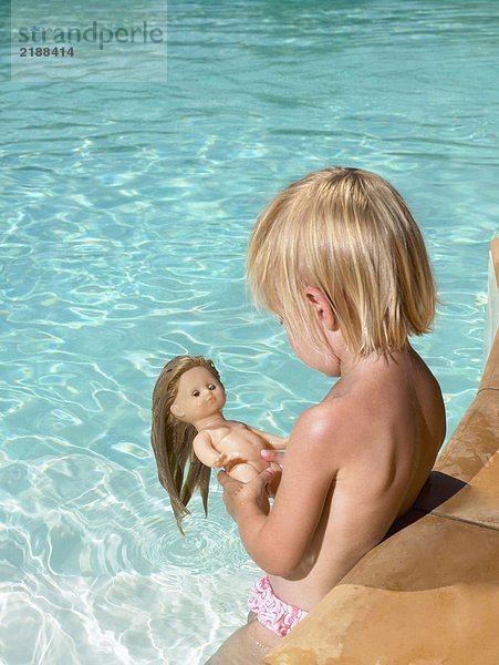 Kleiner Junge spielt mit einer Puppe im Pool.