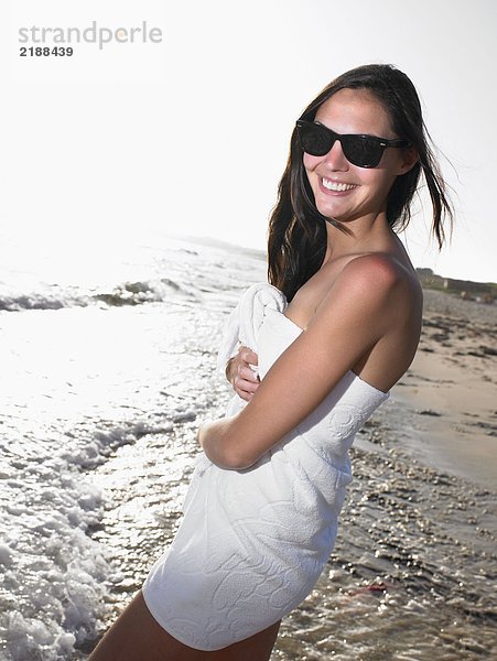 Frau steht in einem Handtuch am Strand und lächelt.