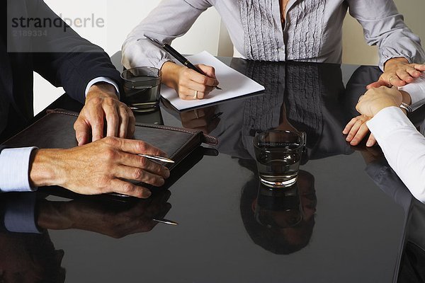 Drei Geschäftsleute mit Reflexionen an einem Tisch arbeiten.