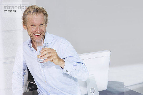 Mann im Büro mit einem Glas Wasser  lächelnd mit Reflexionen.