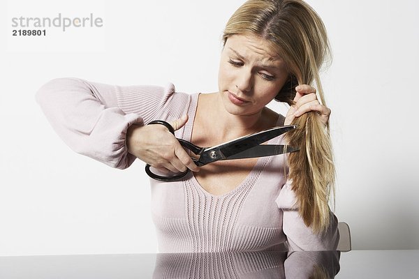 Frau schneidet sich die Haare mit einer Schere.
