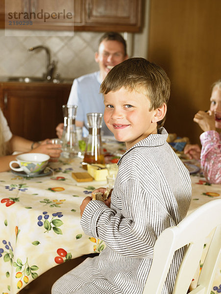 Familie sitzt am Küchentisch und frühstückt lächelnd.