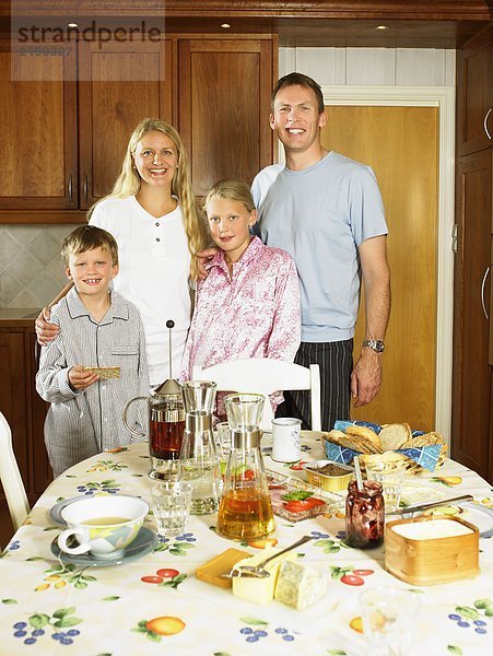 Familie steht in der Küche und lächelt mit Frühstück auf dem Tisch.