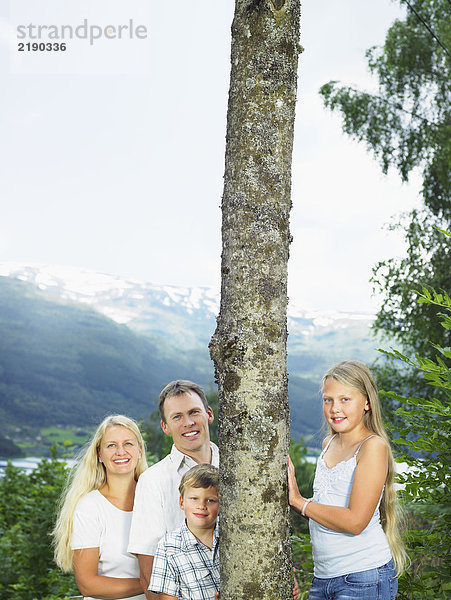 Familie im Freien durch hohen Baum lächelnd.