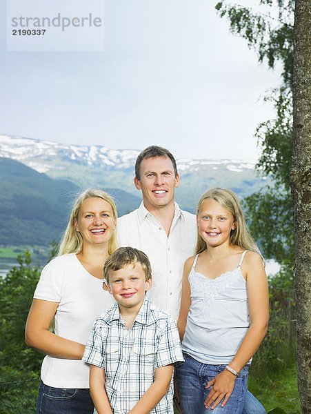 Familie im Freien durch hohen Baum lächelnd.