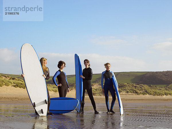 Vier Surferinnen stehen am Strand.