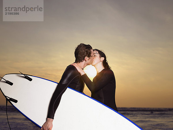 Surferpaar beim Küssen am Strand.