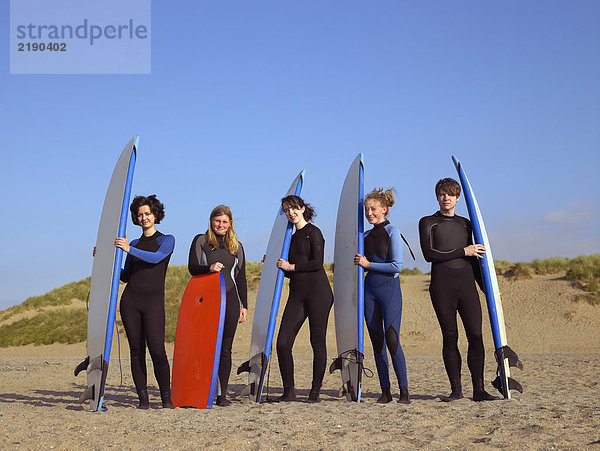 Fünf jugendliche Surfer am Strand.