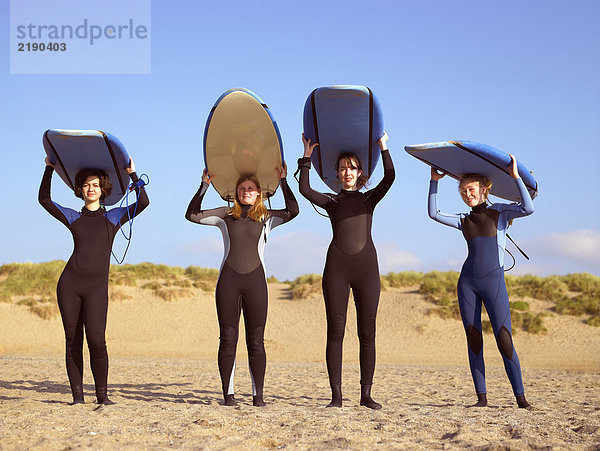 Vier Surferinnen stehen am Strand.