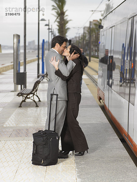 Paare in Business-Outfits  die sich auf dem Bahnsteig neben dem statischen Zug/der Straßenbahn küssen.
