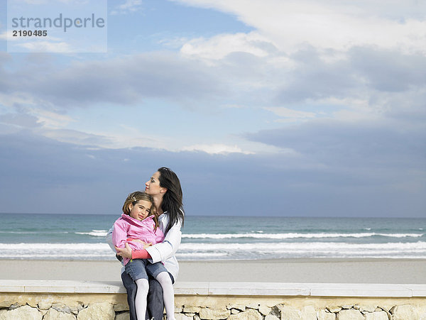 Mutter kuschelnde Tochter (6-8) an der Wand neben dem Strand. Alicante  Spanien.