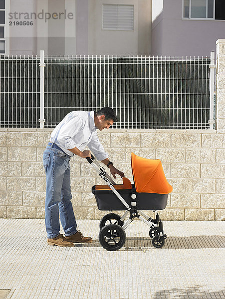Vater schaut in den Kinderwagen auf dem Bürgersteig  Alicante  Spanien
